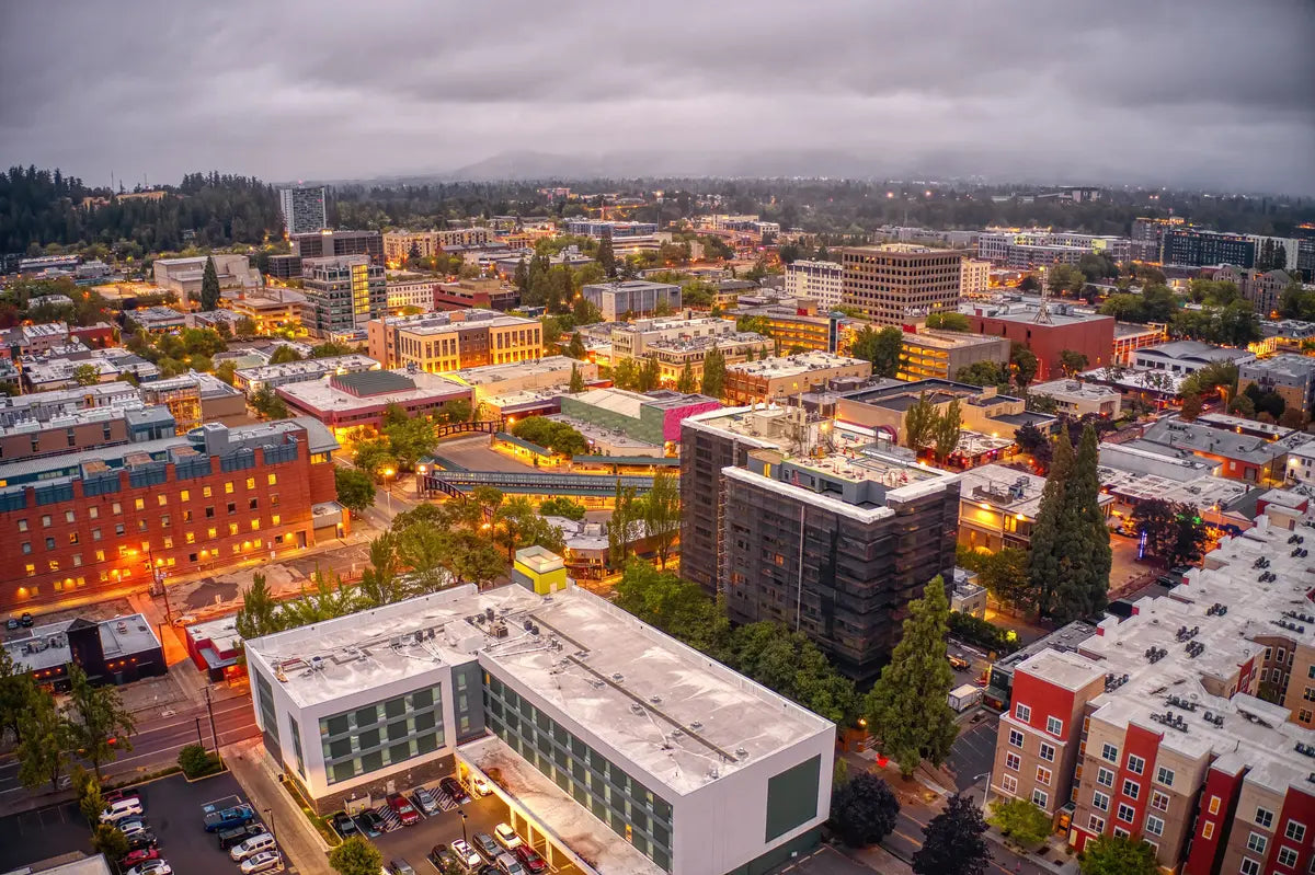 Aerial view of downtown Eugene, Oregon, with illuminated buildings beneath a cloudy sky.
