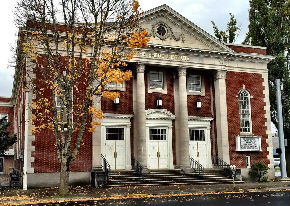 The Shedd Institute building with a red brick facade, white columns and autumn trees.