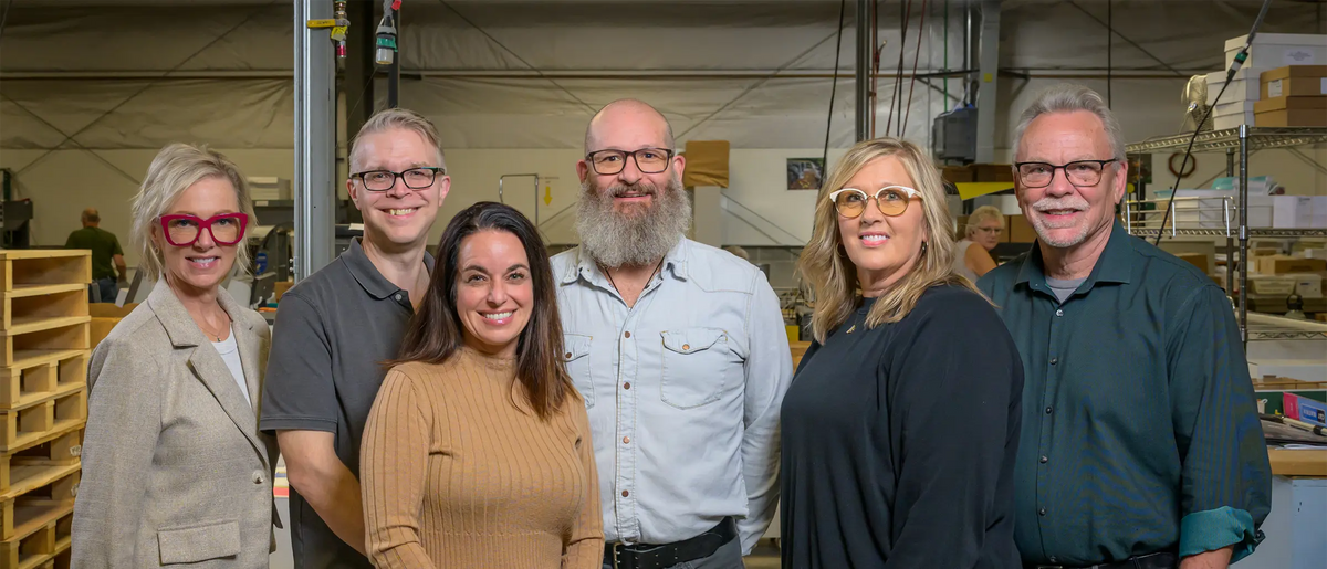 Six Koke Printing team members standing together on the print shop floor.