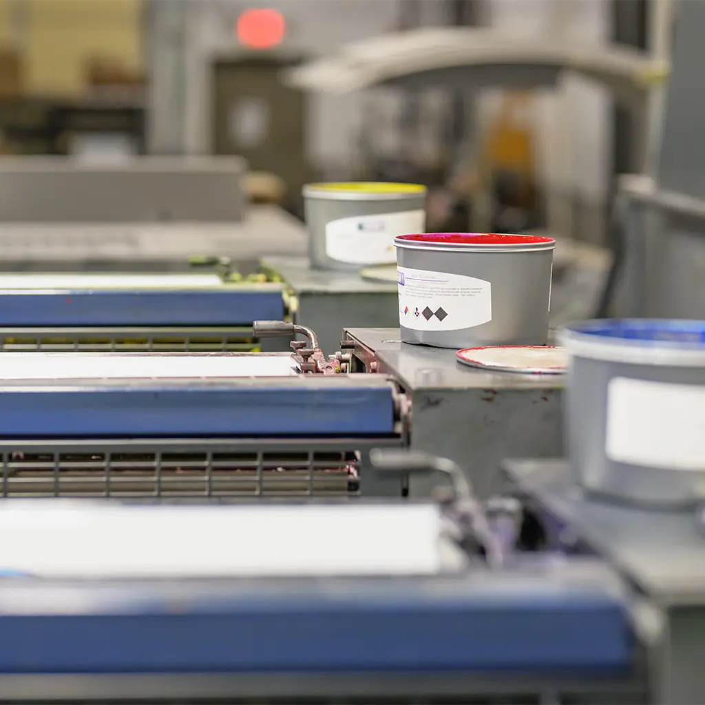 Open containers of colored printing ink beside the rollers of an offset press.
