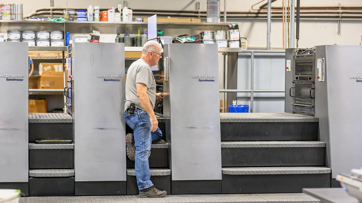 A worker standing between units of a Heidelberg Speedmaster printing press.