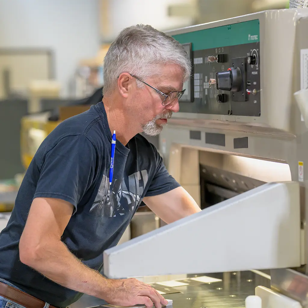 A print shop worker positioning paper in an industrial paper cutter.