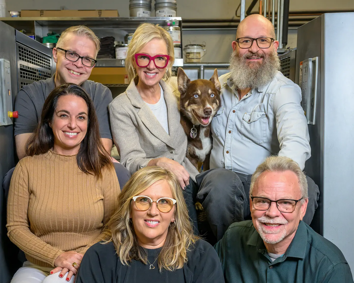 Six Koke Printing team members posing with Thor the dog between printing presses.