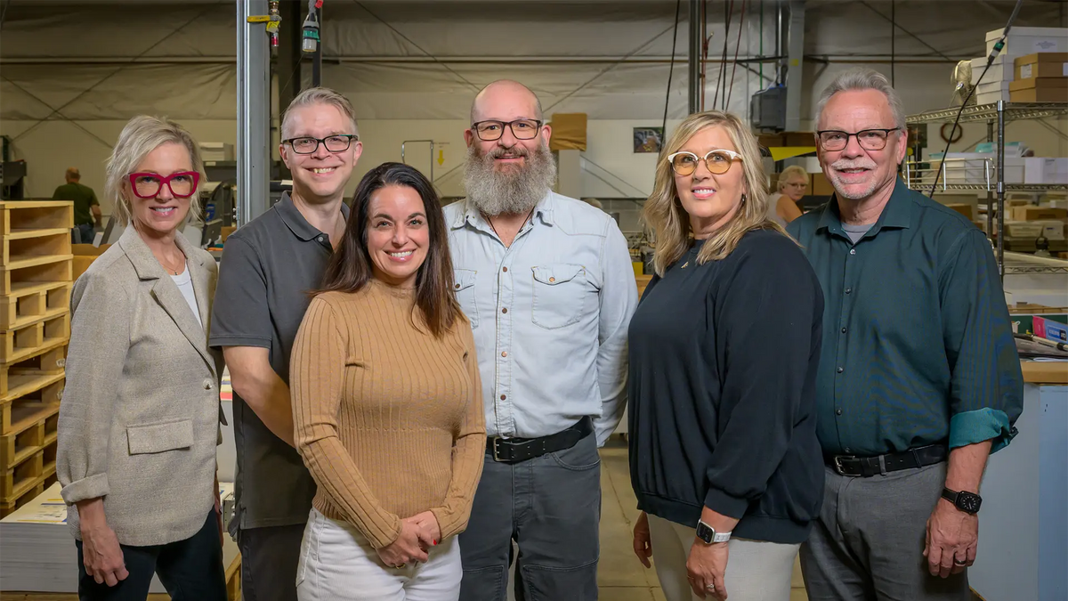 Six Koke Printing team members standing together on the print shop floor.